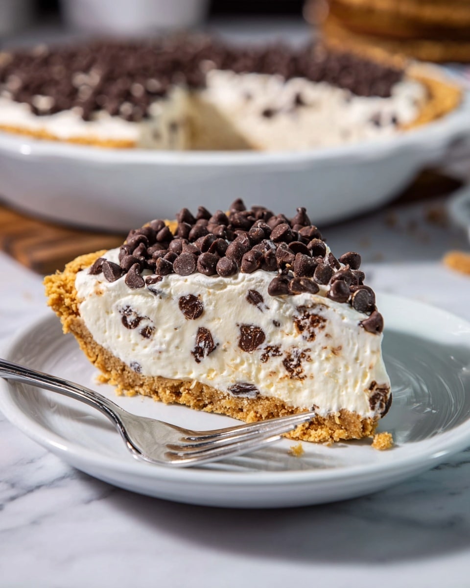 A slice of pie is shown on a white plate with a shiny silver fork beside it. The pie has three visible layers: the bottom layer is a golden brown crust that looks crumbly, the middle layer is thick and creamy white with small dark chocolate chips mixed inside, and the top layer is white cream covered with a generous amount of dark brown mini chocolate chips. The background features a larger pie in a white dish on a white marbled surface. photo taken with an iphone --ar 4:5 --v 7