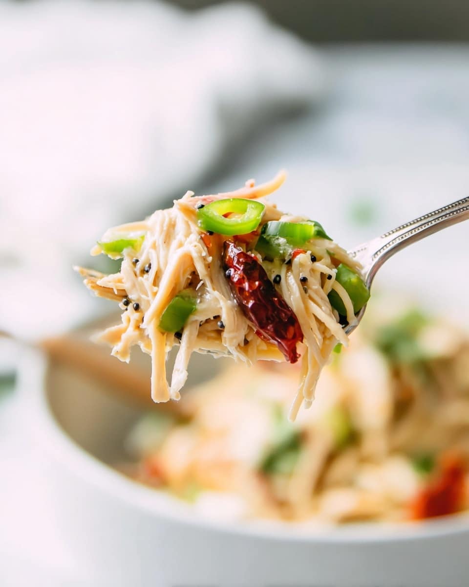 A close-up of a silver fork holding a bite of food with layers including light shredded chicken, thin pale yellow noodles, bright green sliced bell pepper or chili, small black seeds or spices, and a piece of dark red tomato or dried chili, all mixed together with a slightly glossy texture. The background shows a blurred white marbled texture and parts of a white bowl with wooden spoons inside, adding a warm contrast. The focus is on the food on the fork with soft, natural lighting. photo taken with an iphone --ar 4:5 --v 7