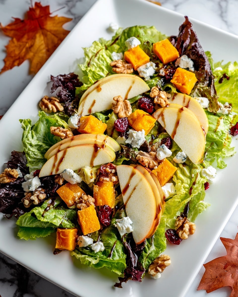 A fresh salad is arranged on a white square plate set on a white marbled surface, sprinkled with autumn leaves around. The base layer consists of various green leafy lettuce, providing a mix of dark and light green colors with a textured, leafy look. On top of the greens, there are thin slices of light yellow-green apples, scattered evenly, showing smooth and firm textures. Bright orange chunks of roasted pumpkin or squash are placed in between the apple slices, adding a soft and slightly shiny texture. Small dollops of white, soft cheese are scattered across the salad, adding a creamy contrast. Dark red dried cranberries and light brown whole walnuts are sprinkled evenly on top, adding varying shapes and a crunchy texture. A dark brown balsamic glaze or dressing is drizzled casually over the entire dish, creating a glossy effect. Photo taken with an iphone --ar 4:5 --v 7
