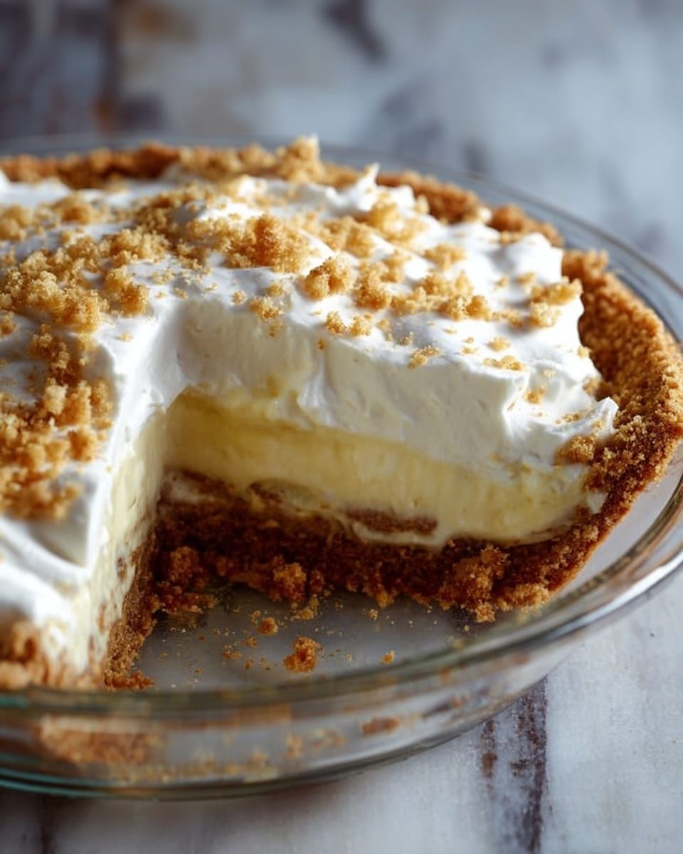 The image shows a close-up of a slice taken from a pie in a clear glass pie dish on a white marbled surface. The pie has three main layers visible: a bottom layer of golden brown crumbly crust, a thick middle layer of smooth pale yellow filling, and a top layer of fluffy white whipped cream sprinkled with light brown crumbled bits. The texture contrasts between the crumbly crust, creamy filling, and soft whipped cream are clear. The lighting highlights the pie's soft and creamy textures. photo taken with an iphone --ar 4:5 --v 7