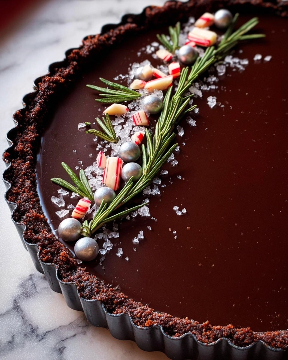 A dark chocolate tart with a smooth, shiny surface in a metal fluted tart pan. The crust around the edge is crumbly and dark brown, contrasting with the glossy almost black chocolate filling. On top, a neat line of white sugar crystals, small silver balls, red and white crushed candy pieces, and fresh green rosemary sprigs run diagonally across the tart. The tart is placed on a white marbled texture surface. photo taken with an iphone --ar 4:5 --v 7