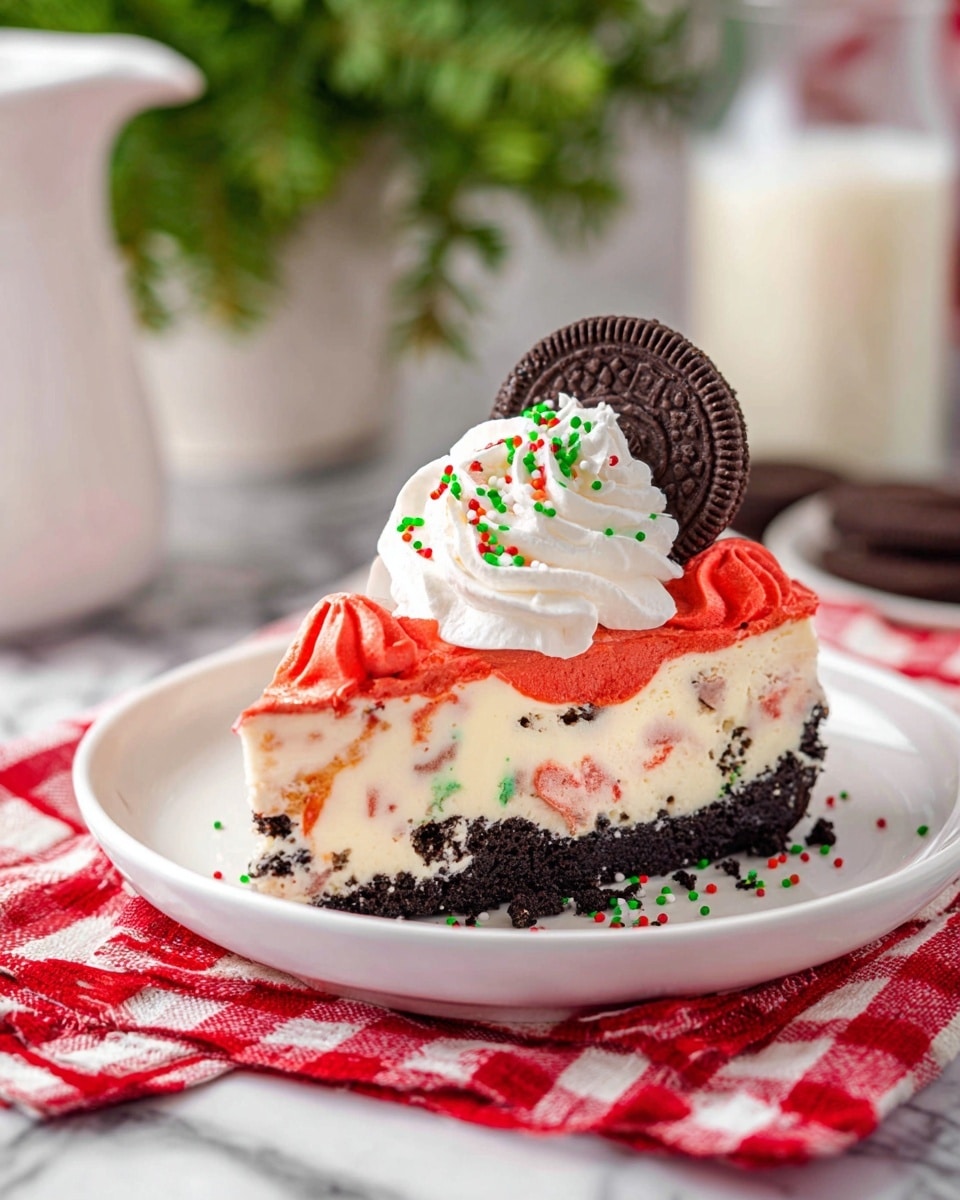 A slice of festive cheesecake sits on a white plate with a layered look: a dark chocolate cookie crumb crust on the bottom, a creamy white cheesecake layer with small red and green bits mixed in the middle, and a bright red swirled topping layer. On top of the cheesecake slice is a dollop of white whipped cream sprinkled with red, green, and white colorful sprinkles, crowned by a small round chocolate cookie. The plate is placed on a red and white checkered cloth on a white marbled surface, with a blurred background showing a glass of milk and a white pitcher with green leaves. Photo taken with an iphone --ar 4:5 --v 7