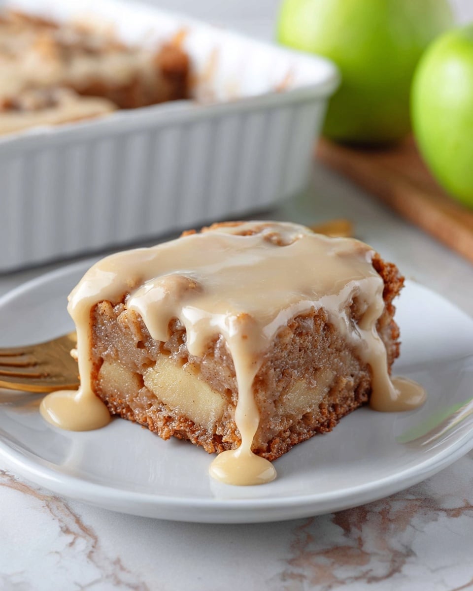A close-up of a square piece of apple dessert served on a white plate, showing two main layers; the bottom layer is a dense, chunky apple cake in light brown with visible pieces of apple and a slightly crispy edge, and the top layer is a thick, creamy beige glaze that drips slowly over the sides of the cake. In the background, there is a white baking dish with more of the dessert and a green apple on a white marbled surface. A gold fork rests near the plate. photo taken with an iphone --ar 4:5 --v 7