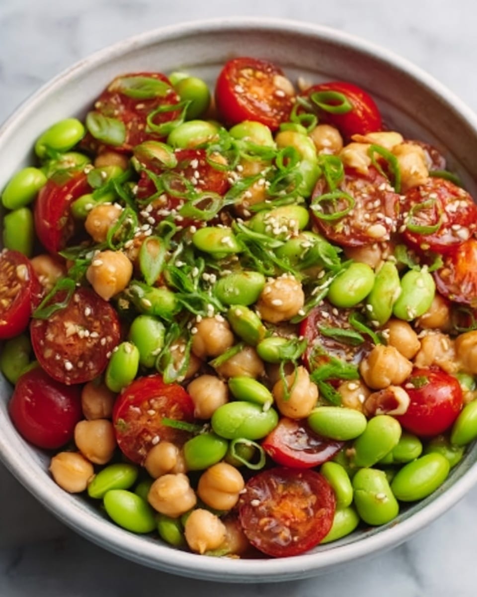 A white bowl filled with a fresh salad showing three main layers: the bottom layer has bright green edamame beans scattered evenly, the middle layer shows golden chickpeas mixed throughout, and the top layer is colorful with halved red cherry tomatoes and finely chopped green herbs sprinkled over all. The salad has a glossy look from a light dressing, and the bowl rests on a white marbled surface. photo taken with an iphone --ar 4:5 --v 7
