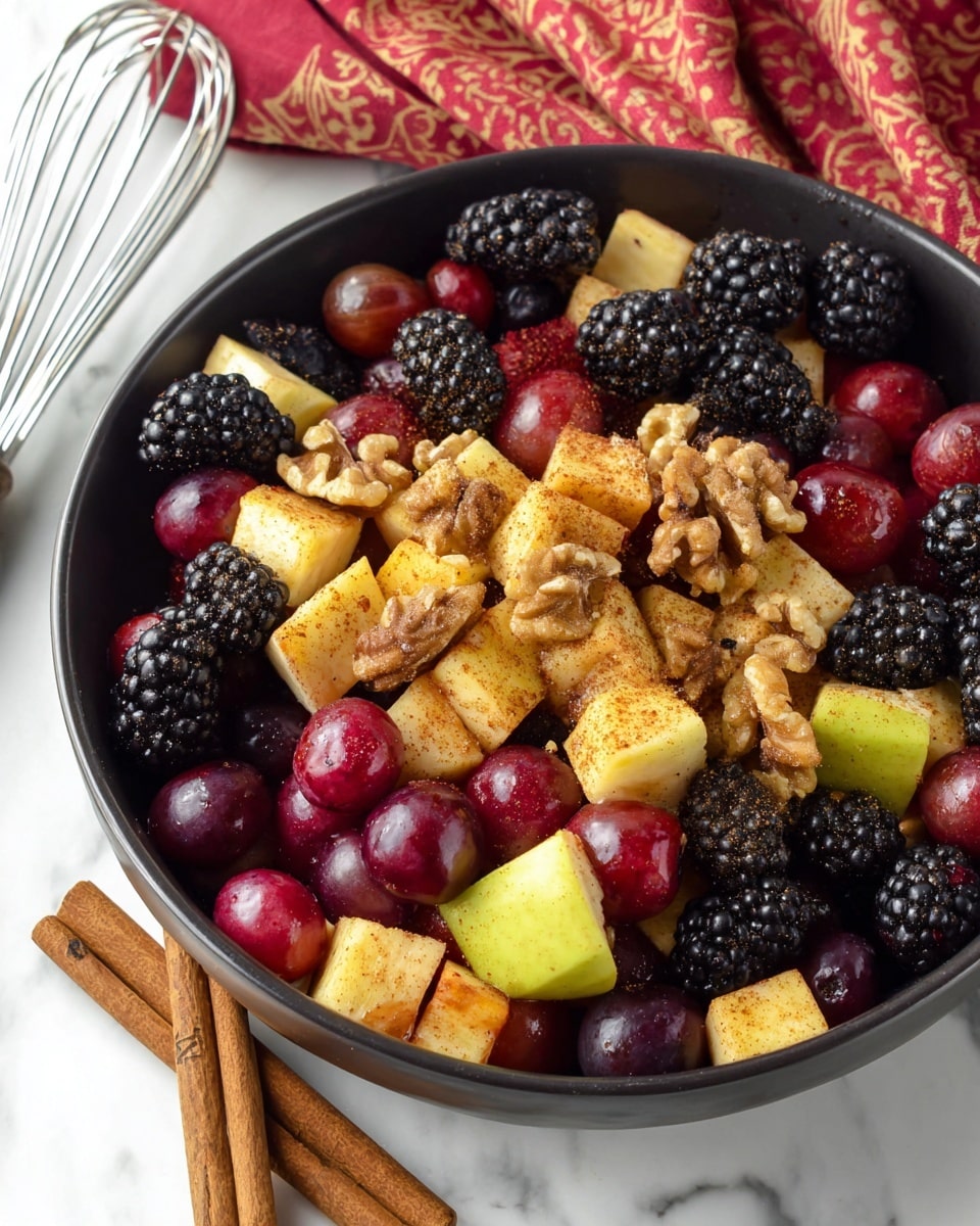 A close-up view of a large dark bowl filled with a colorful fruit salad resting on a white marbled surface, containing three main layers: the bottom layer is made of black blackberries with rich texture, the middle layer has glossy dark red and purple grapes, and the top layer includes chunky light yellow and red apple pieces sprinkled with cinnamon powder, mixed with small clusters of golden-brown walnuts scattered throughout. Nearby the bowl, two cinnamon sticks lay diagonally on the marbled surface, and a silver whisk is partially visible in the upper left corner, topped with a red and beige patterned cloth in the background. photo taken with an iphone --ar 4:5 --v 7