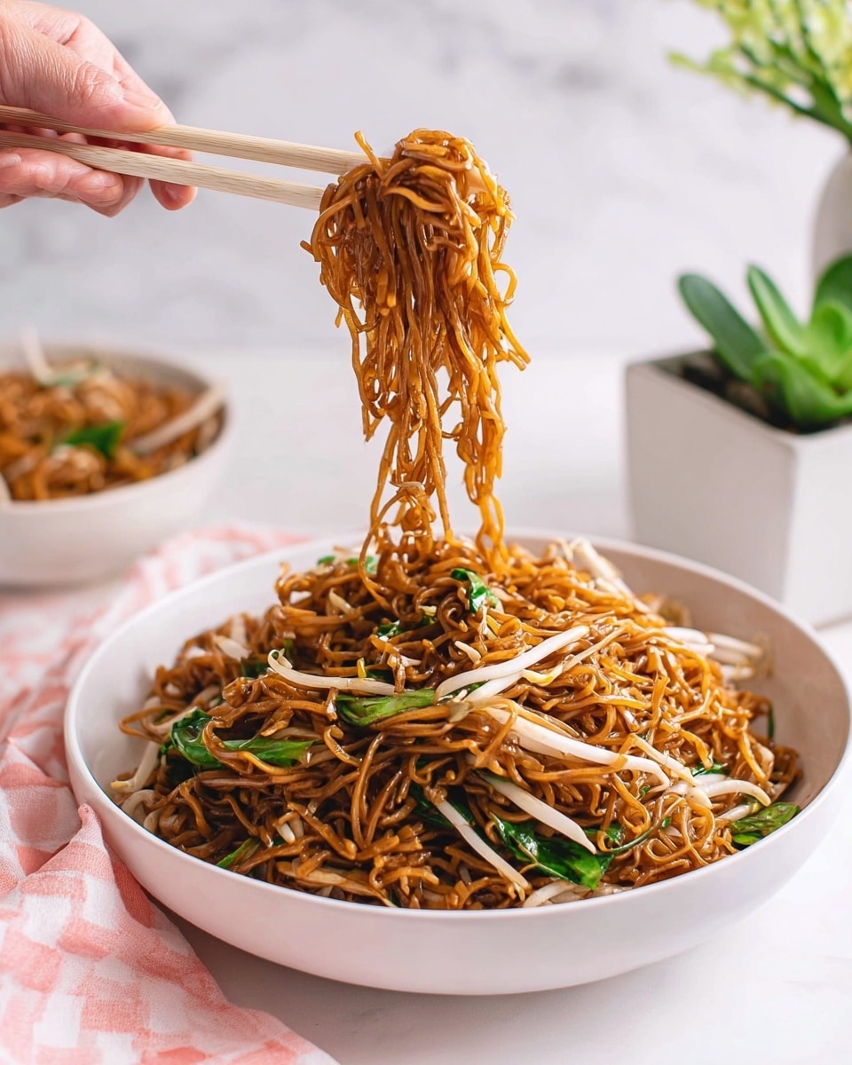 A white bowl filled with thin, shiny brown noodles mixed with white bean sprouts and green leafy vegetables, all stirred together. The noodles have a slightly glossy texture from the sauce, giving them a rich brown color. Above the bowl, a woman's hand holds light beige chopsticks picking up a clump of noodles, lifting them in the air with strands dangling. In the background, there is another white bowl with more noodles and a white marbled surface underneath. A small green plant in a white square pot is visible to the right. A pink and white checkered cloth is placed at the bottom edge of the scene. photo taken with an iphone --ar 4:5 --v 7