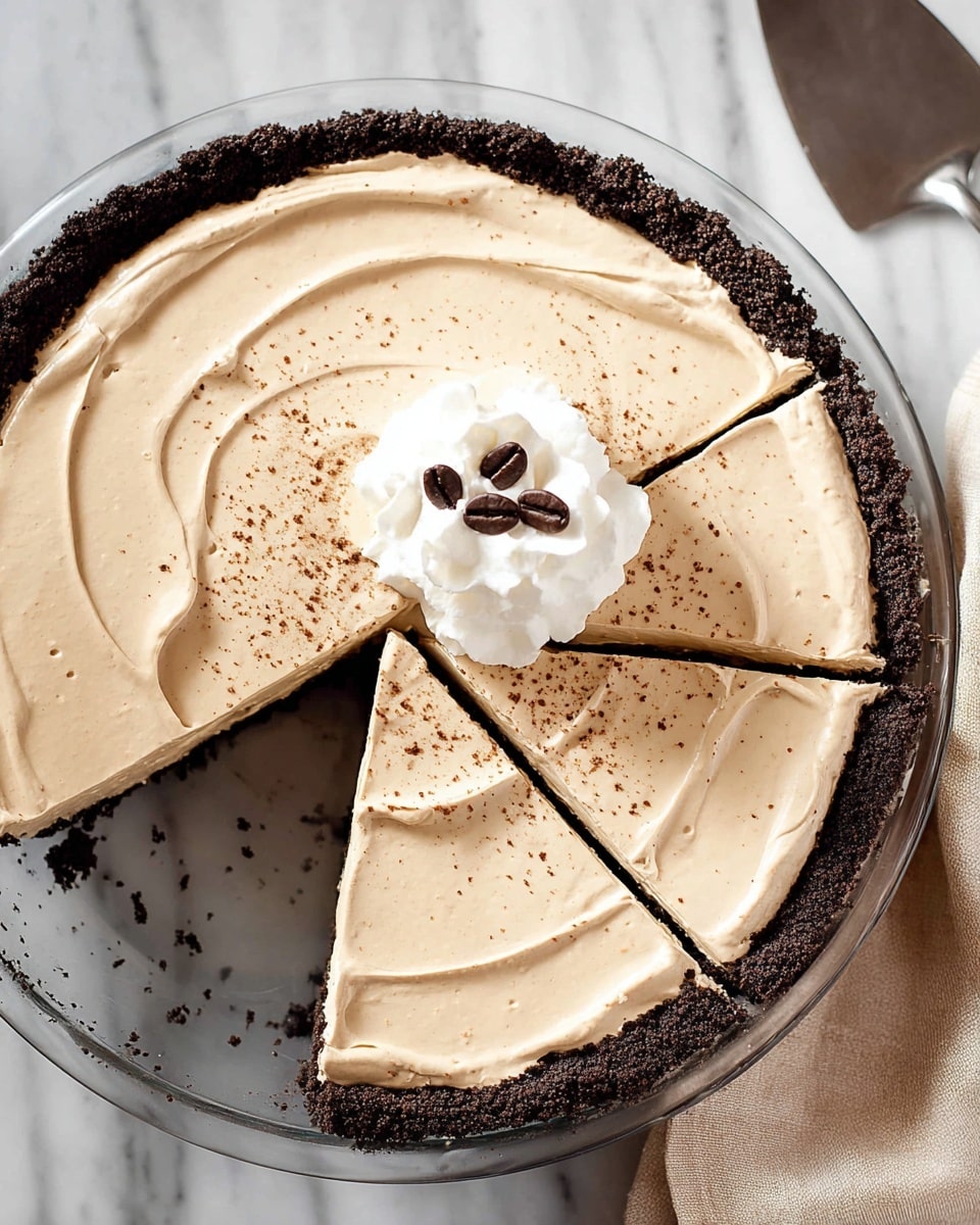 The image shows a creamy pie cut into four slices in a clear glass pie dish resting on a white marbled surface. The pie has two main layers: the bottom layer is a dark brown crumb crust, and the top layer is thick, light brown, smooth cream with gentle swirled patterns. There is a dollop of white whipped cream in the center, topped with three dark coffee beans. Light brown specks are sprinkled lightly over the creamy top layer, adding texture. A silver pie server is placed next to the dish. Photo taken with an iphone --ar 4:5 --v 7
