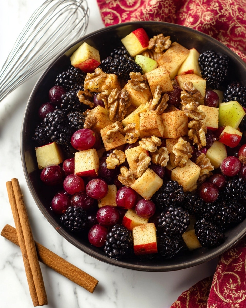 A close-up image of a fruit salad in a white bowl with a white marbled surface underneath; the salad shows three layers: large red and dark purple grapes that are shiny and round, mixed with blackberries that have a bumpy texture; light yellow and red apple pieces cut into cubes covered with a light coating of cinnamon powder adding a light brown speckled texture; and scattered in between are crunchy brown pecans, some whole and some in halves. The background includes a wire whisk and a red cloth with a beige pattern. photo taken with an iphone --ar 4:5 --v 7