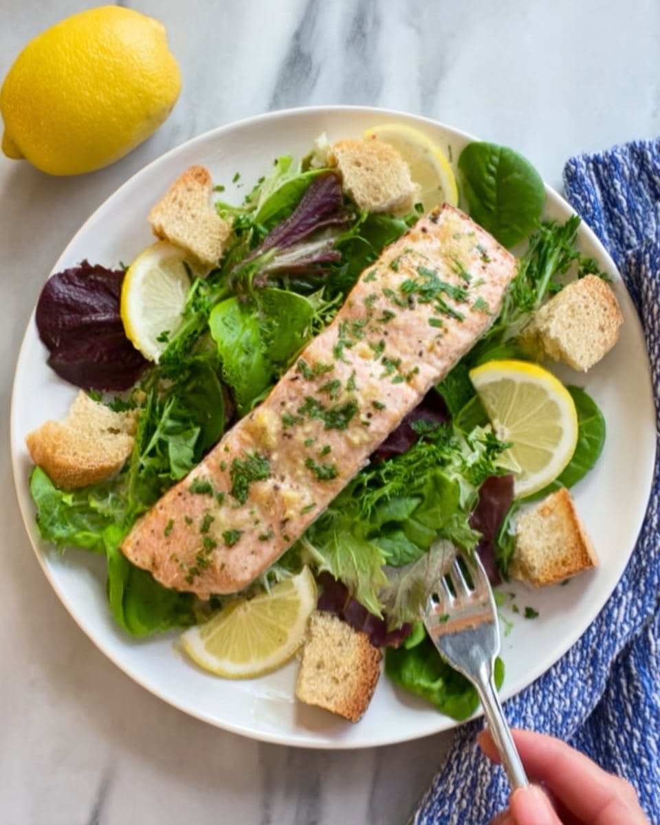 A white plate holds a green salad with fresh leafy greens and large lemon wedges placed around the edges. On top of the salad sits a cooked salmon fillet, light pink with a seasoned crust speckled with green herbs. The salmon is positioned in the center of the plate, slightly overlapping the greens beneath it. The photo is taken with a woman's hand holding the plate on the side, set against a white marbled surface. Photo taken with an iphone --ar 4:5 --v 7
