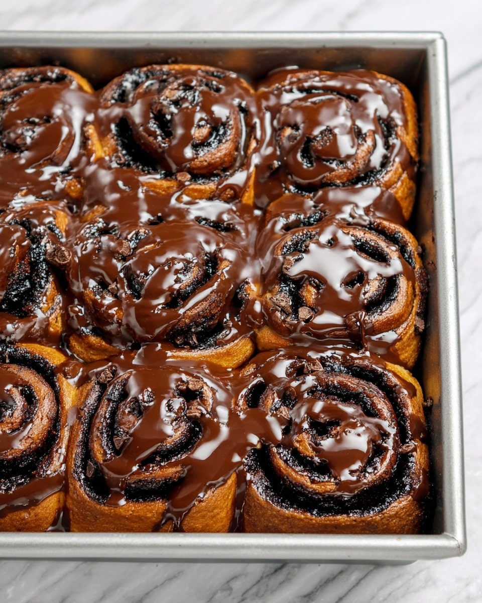 The image shows a baking pan filled with eight cinnamon rolls arranged closely together. Each roll has a dark brown dough with visible spiral layers of almost black filling, creating a rich contrast. The rolls are topped with a glossy, light brown caramel sauce drizzled unevenly over the whole surface, some dripping down the sides of the pan. The pan sits on a white marbled surface, enhancing the focus on the warm-toned cinnamon rolls. photo taken with an iphone --ar 4:5 --v 7