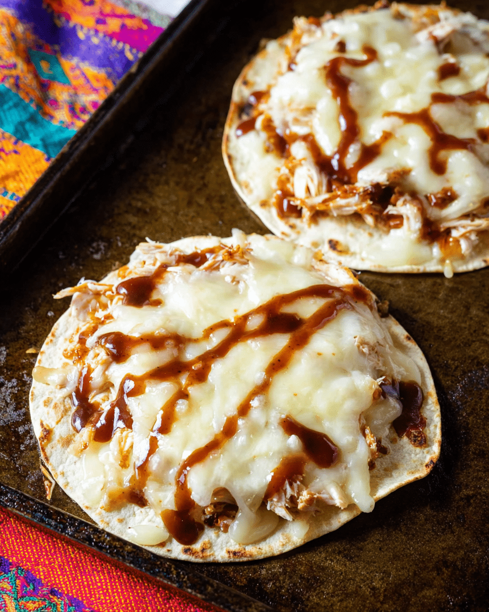 The image shows two small flat round tortillas placed on a dark baking tray with melted white cheese covering each one in a thick layer, soft and creamy in texture. Below the cheese, bits of shredded chicken can be seen slightly browned, giving a rough texture under the smooth cheese layer. On the top, dark brown sauce is drizzled unevenly in patches adding gloss and a rich contrast. The tortillas have slightly crisp edges and the background features a white marbled texture with a colorful fabric edge in the bottom foreground, giving a warm and rustic feel. photo taken with an iphone --ar 4:5 --v 7