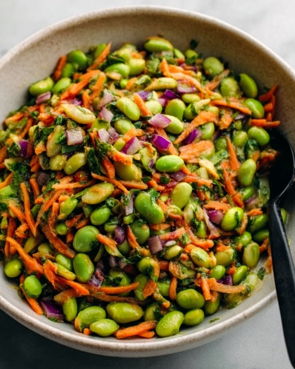 A close-up view of a white bowl filled with a colorful salad made of bright green edamame, orange shredded carrots, small purple onion pieces, and finely chopped green herbs, all mixed together with a slightly glossy texture. The bowl is on a white marbled surface, and a black spoon is partly visible on the right side inside the bowl. The image showcases a fresh and vibrant mix with several visible layers of different vegetable textures and colors. Photo taken with an iphone --ar 4:5 --v 7