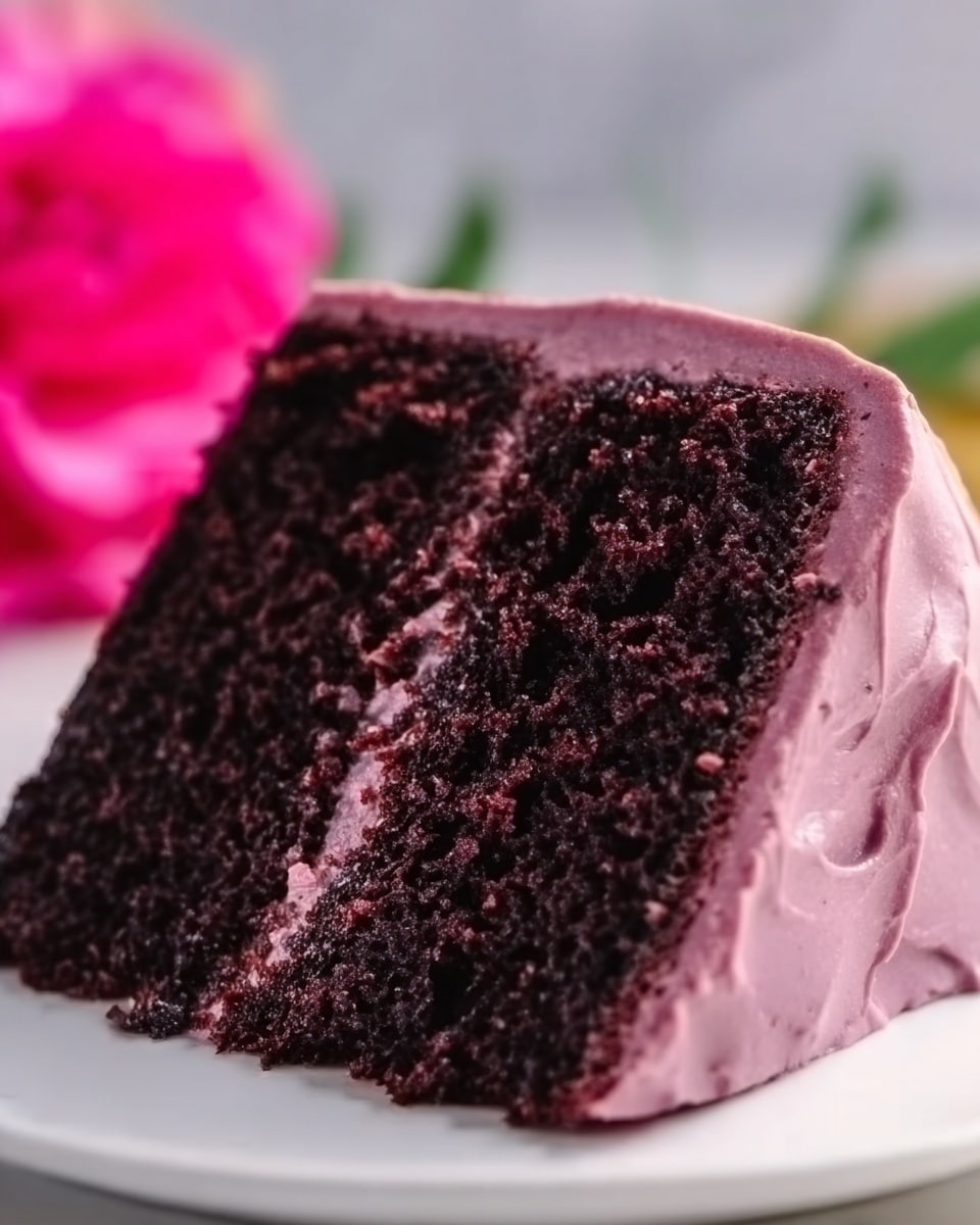 A close-up of a tall two-layer dark chocolate cake with a smooth purple icing covering the outside and a thick layer of purple frosting between the two moist, rich chocolate layers. The surface of the cake has a creamy texture, and it sits on a white marbled surface with a blurred bright pink flower in the background. The slice is cut cleanly, showing the dense, dark cake and smooth frosting clearly. Photo taken with an iphone --ar 4:5 --v 7