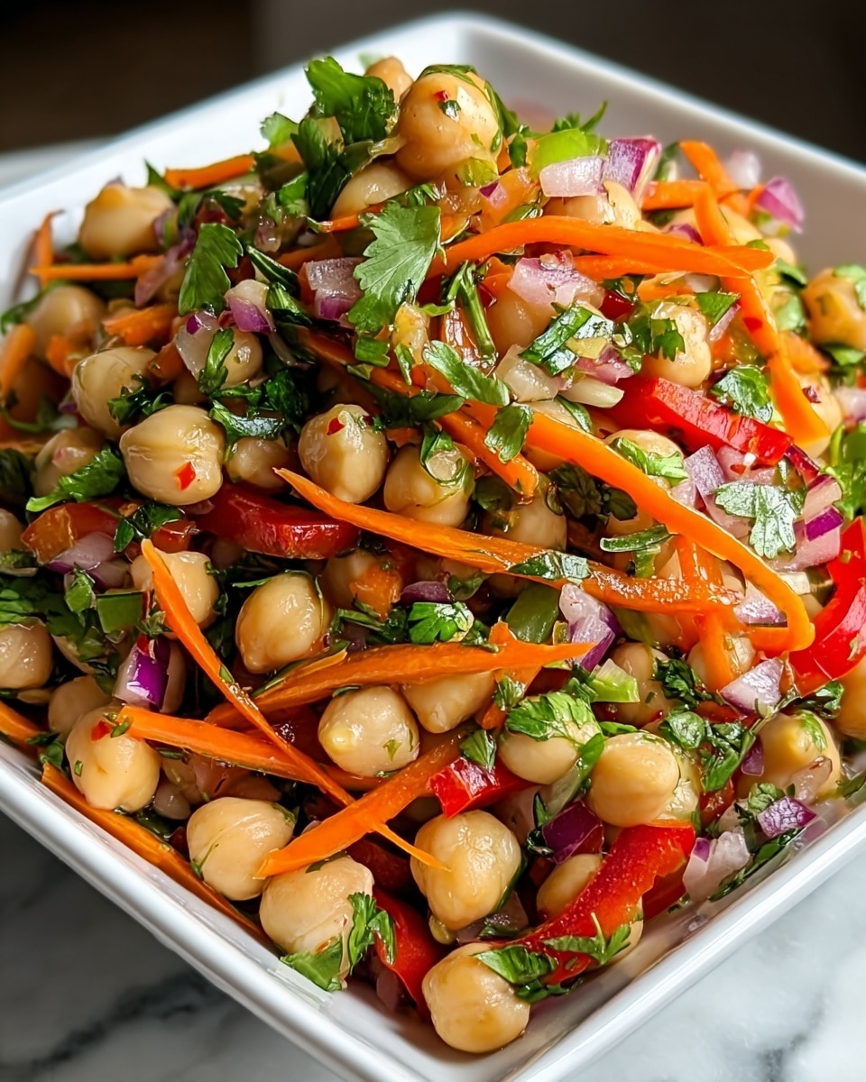 A close-up of a chickpea salad served in a white square bowl, filled with three main layers: the bottom layer has whole beige chickpeas, the middle layer contains thin strips of bright orange carrots and red bell peppers, and the top layer is scattered with fresh green cilantro leaves and small pieces of red onion seen throughout. The textures range from smooth chickpeas to crunchy vegetables, all mixed together with a light glossy dressing that makes the colors pop, placed on a white marbled surface. Photo taken with an iphone --ar 4:5 --v 7