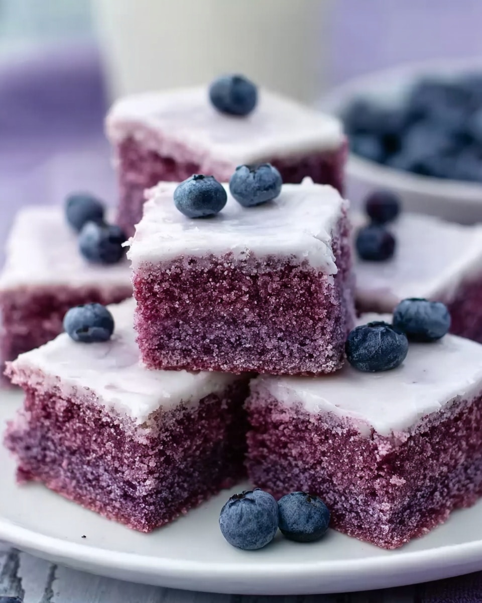 The image shows a white plate filled with square purple cake pieces, each topped with a thin layer of pale white icing. The cake layers have a dense, moist texture and a rich purple color. The icing looks smooth and slightly glossy, covering only the top surface of each piece. Around the plate, fresh blueberries with deep blue and purple hues are scattered on a white marbled surface. In the background, more purple cake squares are blurred, sitting on a white marbled surface. Photo taken with an iphone --ar 4:5 --v 7