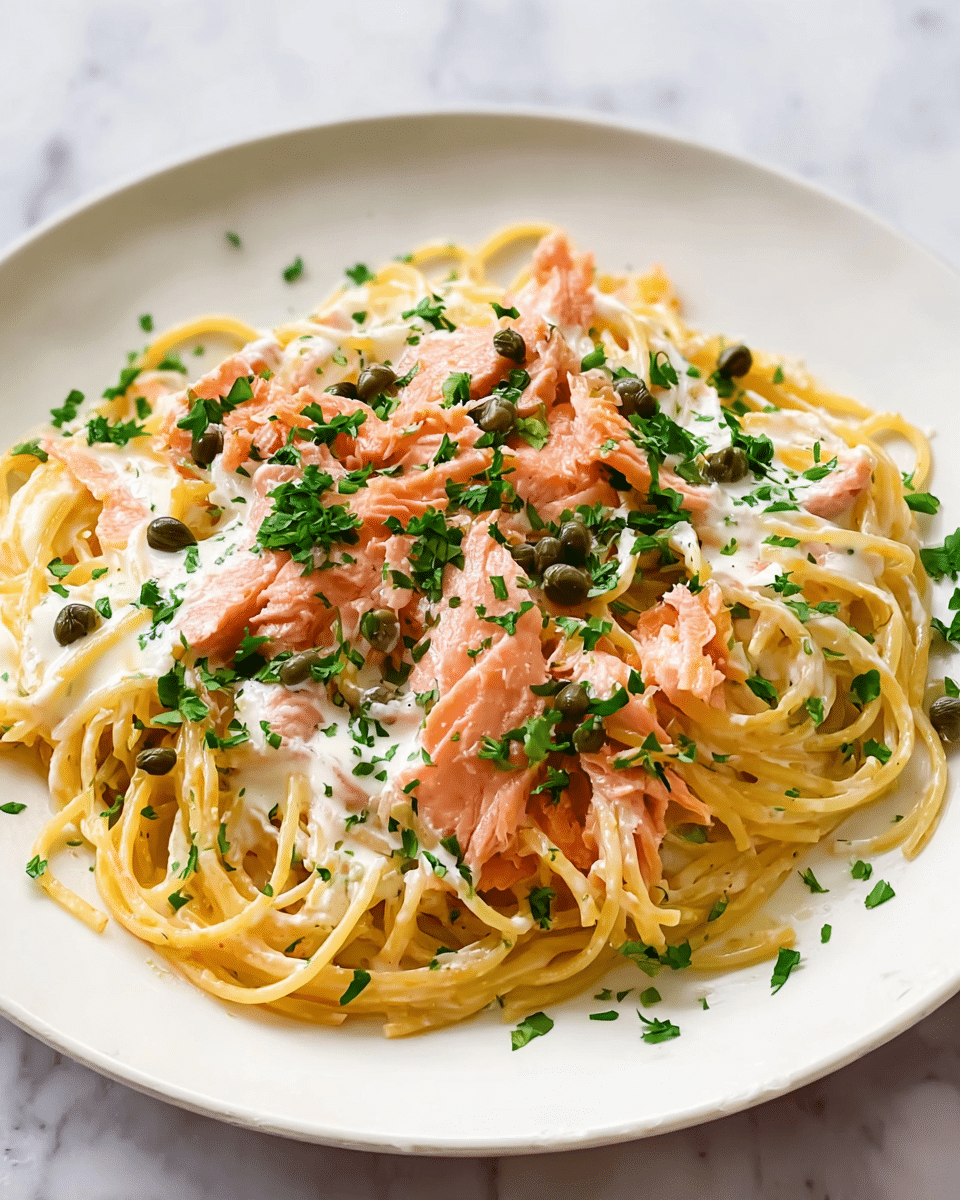 A white plate holds a dish of creamy pasta made of long, thin spaghetti noodles mixed with pink pieces of salmon. The pasta is coated in a smooth, pale cream sauce that wraps around each strand. Small, dark green capers are scattered on top, adding texture and color contrast. Bright green chopped parsley is sprinkled evenly over the dish, giving it a fresh look. The pasta is layered in a loose pile, showing the creamy sauce, salmon flakes, and garnishes clearly against the white plate and white marbled surface. Photo taken with an iphone --ar 4:5 --v 7