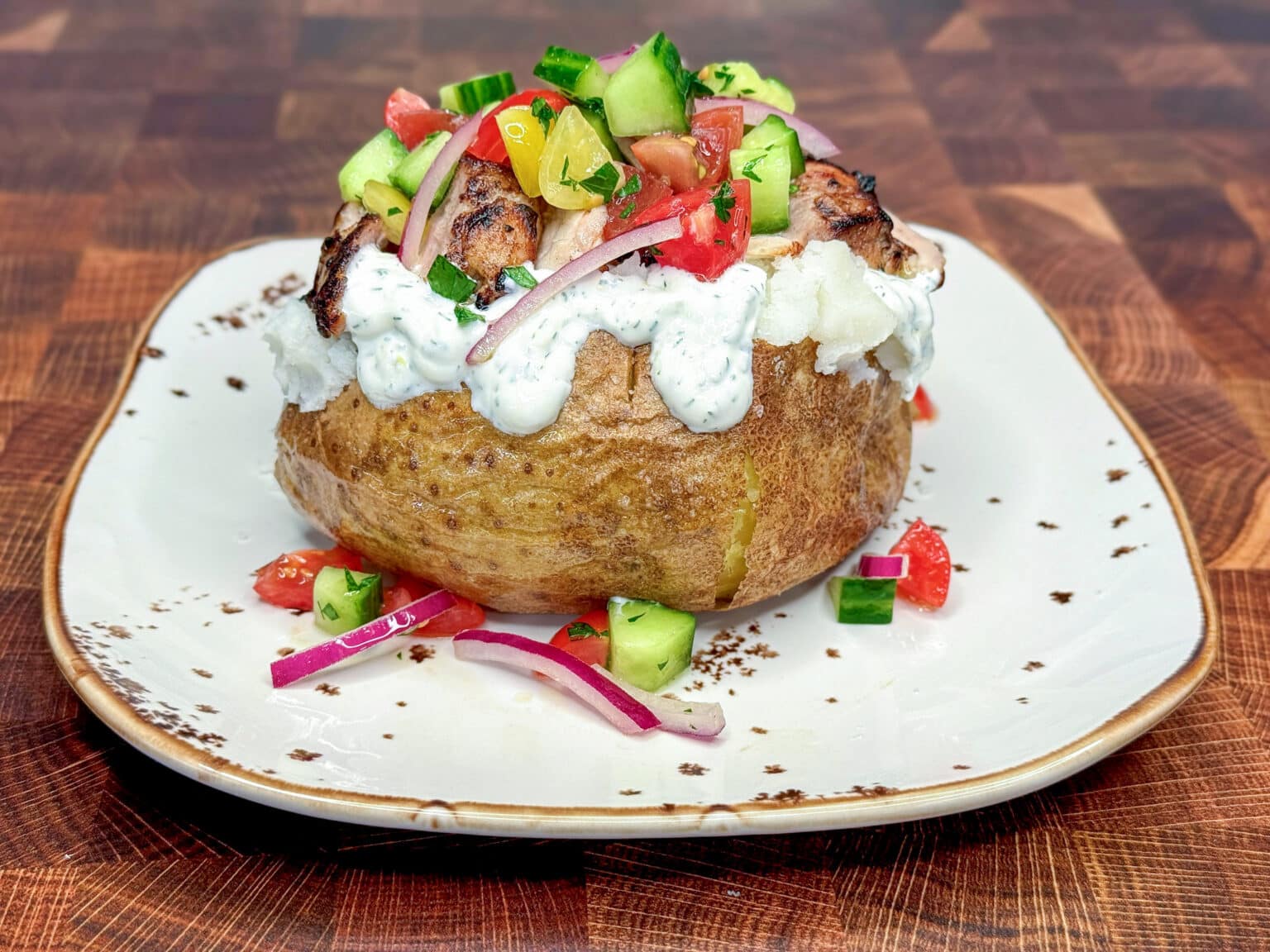 A baked potato with a crispy brown skin sits in the center of a white plate with a rustic rim, placed on a white marbled surface. The potato is opened and fluffy white inside. On the potato, there is a thick layer of creamy white sauce with green herbs mixed in, topped with pieces of grilled meat that have a slightly charred, brown surface. Above the meat, there is a fresh salad made of diced green cucumber, red and yellow tomatoes, and thin slices of purple onion mixed with chopped green herbs. Some pieces of the salad and onion are scattered around the base of the potato on the plate. photo taken with an iphone --ar 4:5 --v 7