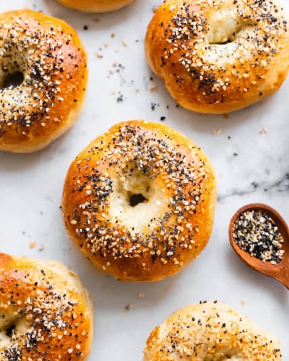The image shows several golden brown bagels on a white marbled surface, each topped with a mix of white sesame seeds and black seeds. The bagels are round with a soft, shiny texture and slightly uneven surfaces that show they are freshly baked. A wooden spoon filled with a seasoning mix of black and white seeds is placed nearby to the right. The scene is bright and clean, highlighting the contrast between the golden bagels and the white background. Photo taken with an iphone --ar 4:5 --v 7