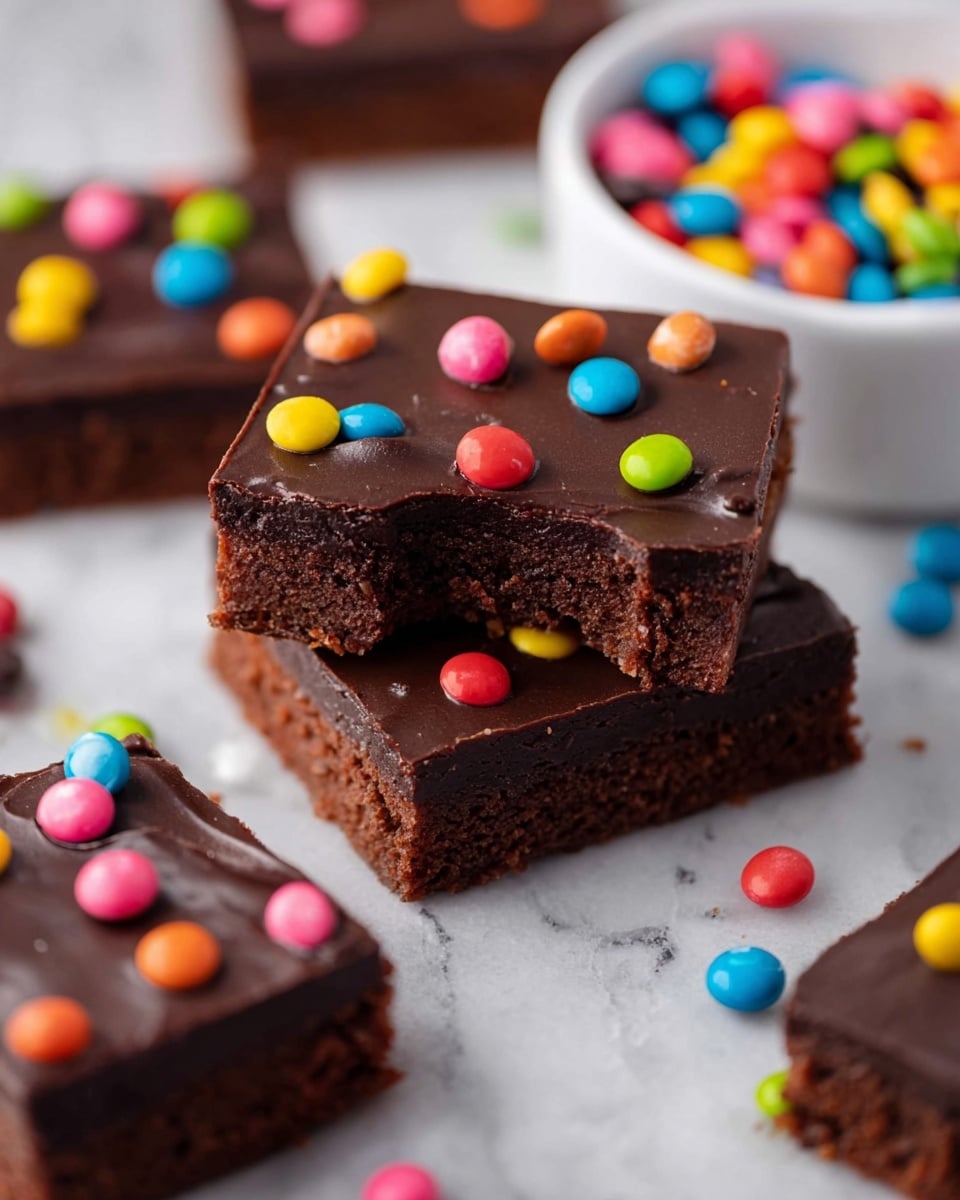 The image shows several square brownie pieces stacked and spread out on a white marbled surface. Each brownie has two visible layers: a dense, dark brown base layer with a slightly crumbly texture, and a smooth, glossy dark chocolate ganache layer on top. The ganache is decorated with small, colorful round candy sprinkles in bright colors like pink, blue, red, yellow, green, and orange, scattered unevenly on the surface. One brownie piece in the front has a bite taken out, revealing the thick, rich texture of the bottom layer. In the background, there is a white bowl filled with similar colorful candy sprinkles. Photo taken with an iphone --ar 4:5 --v 7